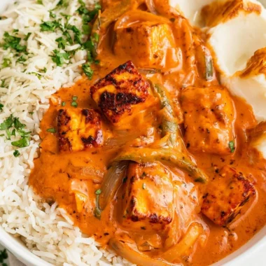 A bowl of cottage cheese tikka curry garnished with fresh cilantro and spices