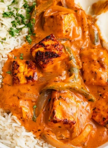 A bowl of cottage cheese tikka curry garnished with fresh cilantro and spices