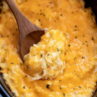 A serving of creamy crockpot cheesy potatoes topped with cheese and herbs.