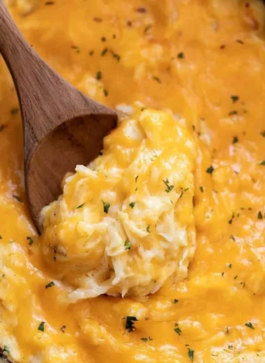 A serving of creamy crockpot cheesy potatoes topped with cheese and herbs.