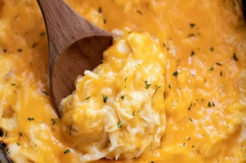 A serving of creamy crockpot cheesy potatoes topped with cheese and herbs.