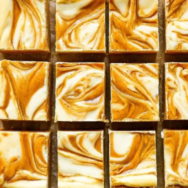 Pumpkin cream cheese cheesecake bars topped with whipped cream in a dish.