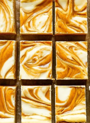 Pumpkin cream cheese cheesecake bars topped with whipped cream in a dish.