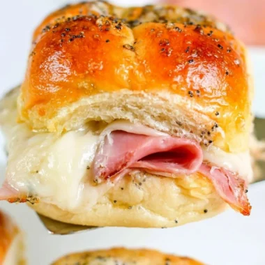 Baked ham and cheese sliders served on a platter with herbs and condiments.