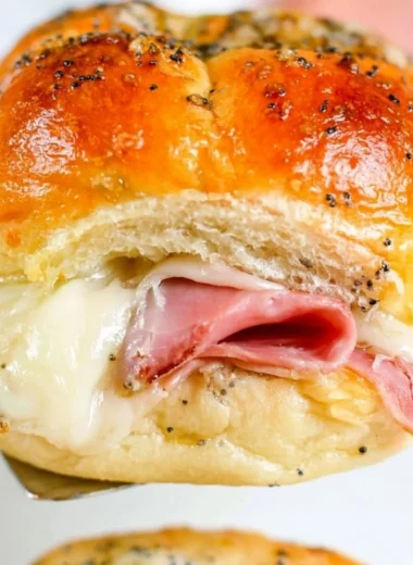 Baked ham and cheese sliders served on a platter with herbs and condiments.