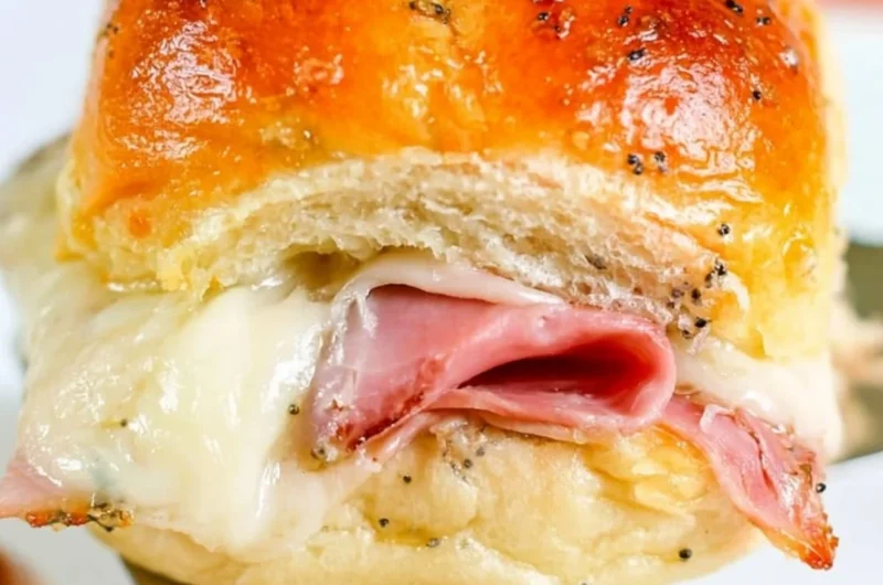 Baked ham and cheese sliders served on a platter with herbs and condiments.