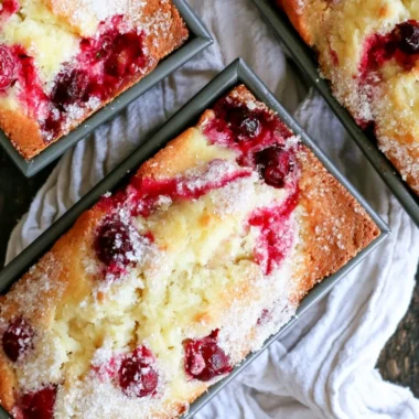 Loaf of cozy cranberry quick bread garnished with fresh cranberries.