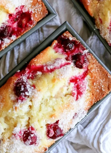 Loaf of cozy cranberry quick bread garnished with fresh cranberries.
