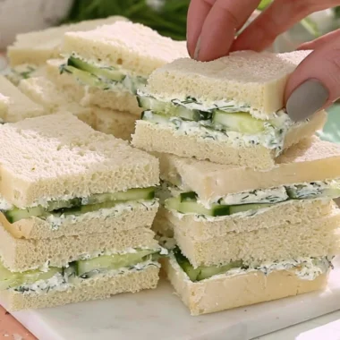 Plate of cucumber sandwiches with fresh herbs and a side of tea