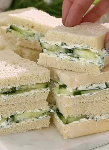 Plate of cucumber sandwiches with fresh herbs and a side of tea